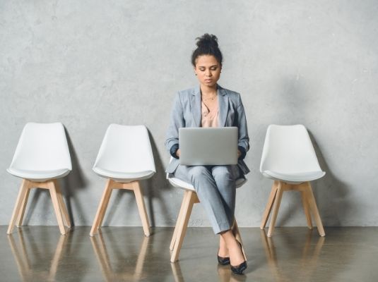 Five Pro’s to Working For an Agency image of Woman sitting in a row of white chairs looking up agency on her computer