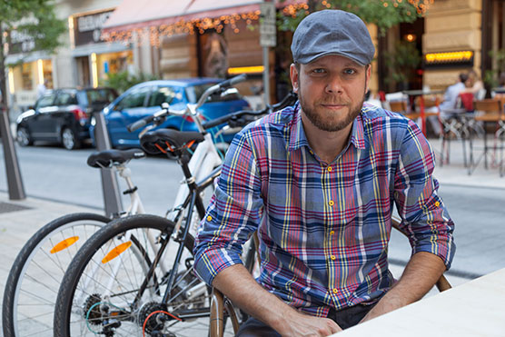 Staff member outside and seated near bikes and wearing a hat and smiling