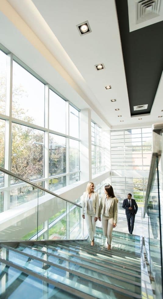 Two women walking up a corporate staircase with open windows to one side.