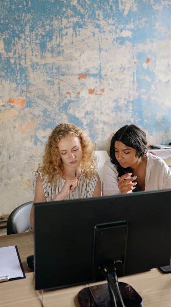 Communications Staffing Agency with two women working on a computer - light blue wall behind them.