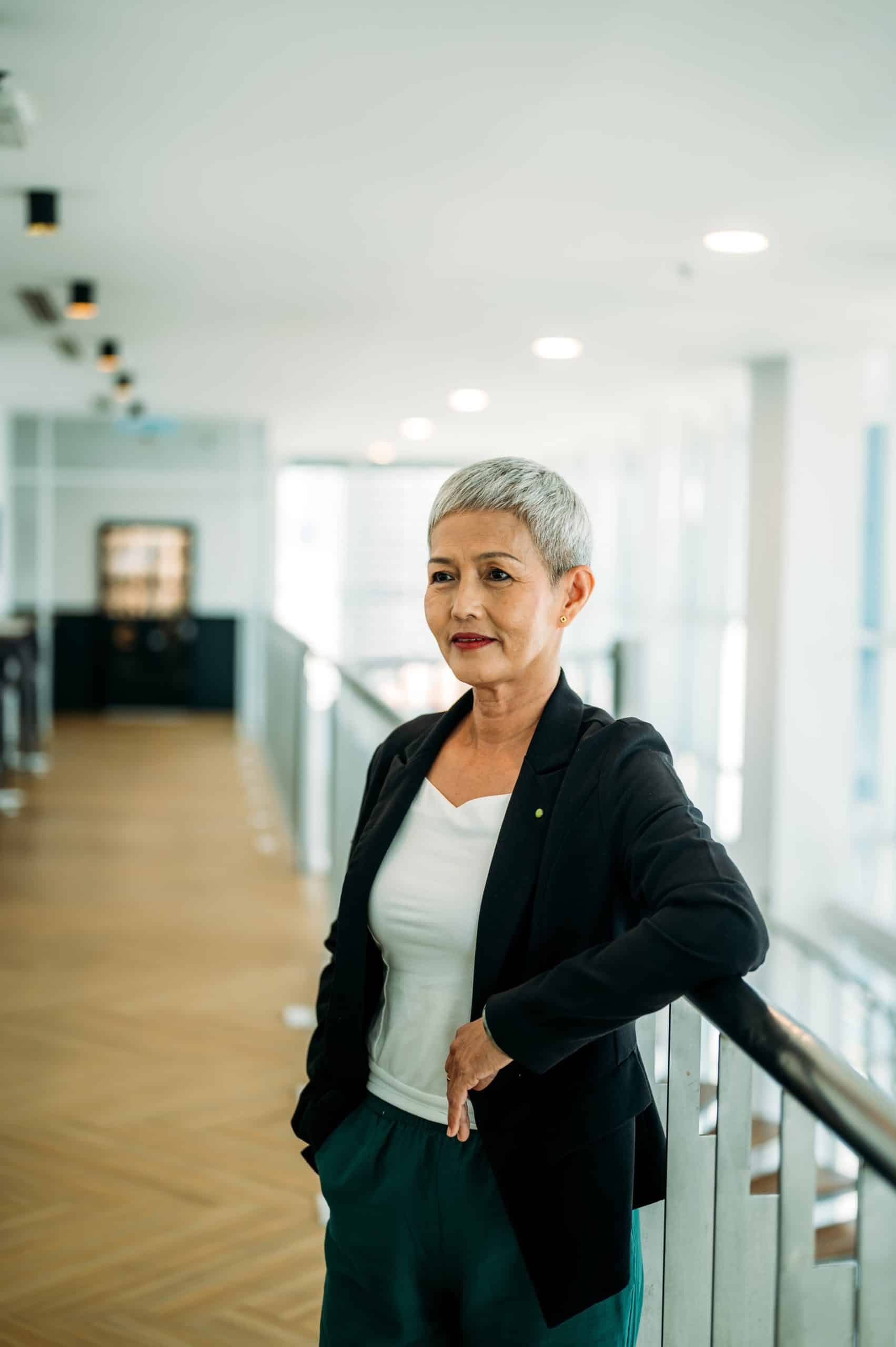 Finance Controller and Confident stylish Asian mature middle aged woman standing at modern workplace. Stylish older senior businesswoman, 60s gray-white haired lady executive leader manager looking away camera in office, portrait.