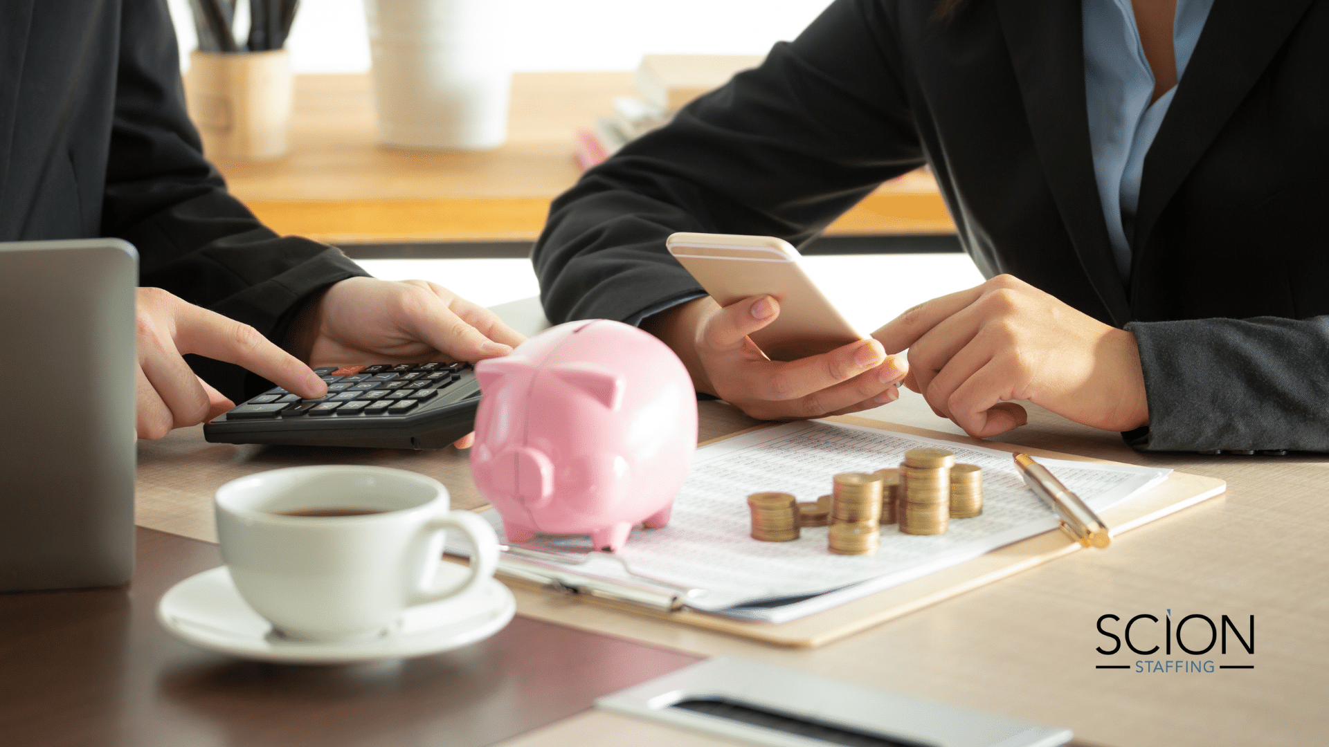 10 Essential Skills Every Finance Manager Should Have - two finance managers sitting at table going over financial numbers with a piggy bank, coins, and a cup of coffee